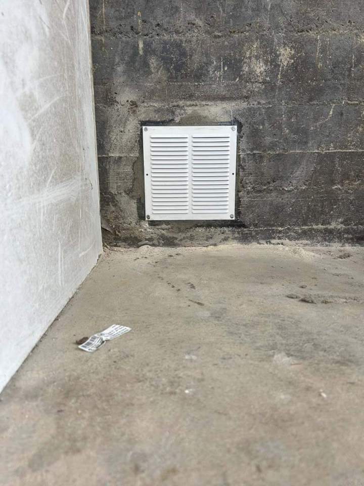 Grille de ventilation blanche fixée à un mur de fondation en blocs de béton rugueux Josselin