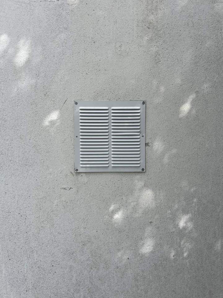 Grille d'aération carrée fixée sur un mur extérieur en stuc Josselin