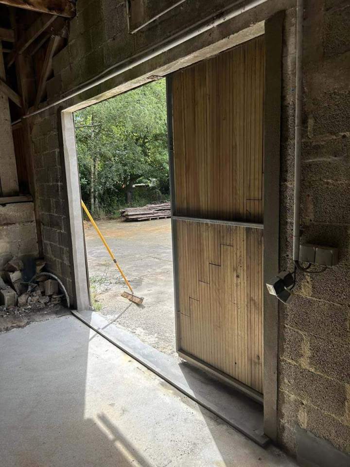 Porte de garage en bois à deux battants intégrée dans un mur en blocs de béton Josselin