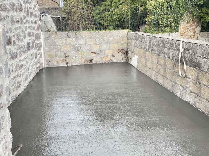 Dalle de béton fraîchement coulée, entourée de murs de pierre et parpaings Josselin